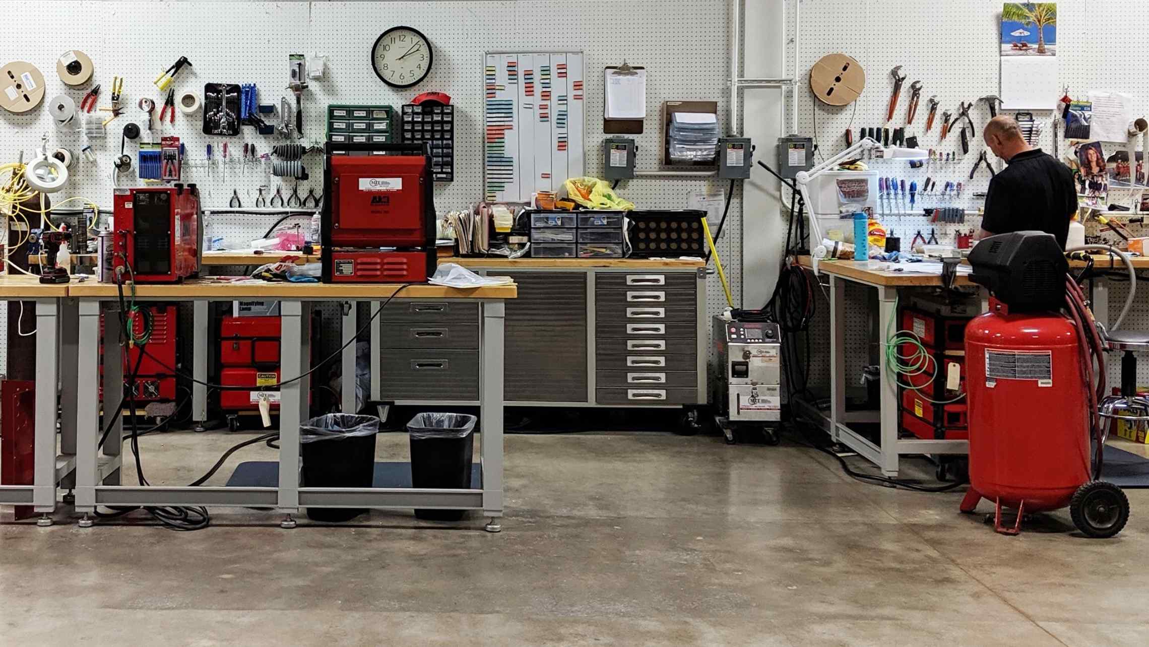 A fabricator using an orbital welding machine in a clean, well-lit workshop with organized tool storage in the background